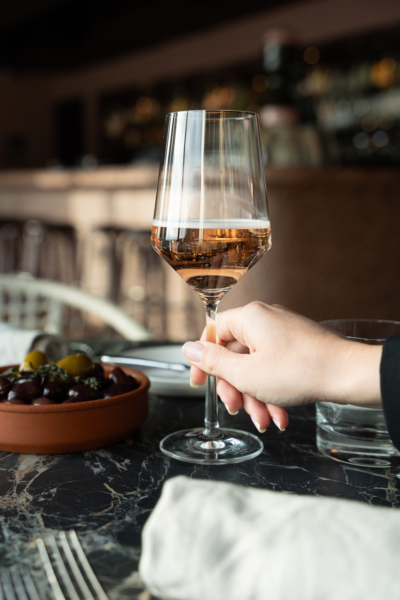 Weinglas mit alkoholfreiem Oolong Orange mit feiner Perlage neben Oliven